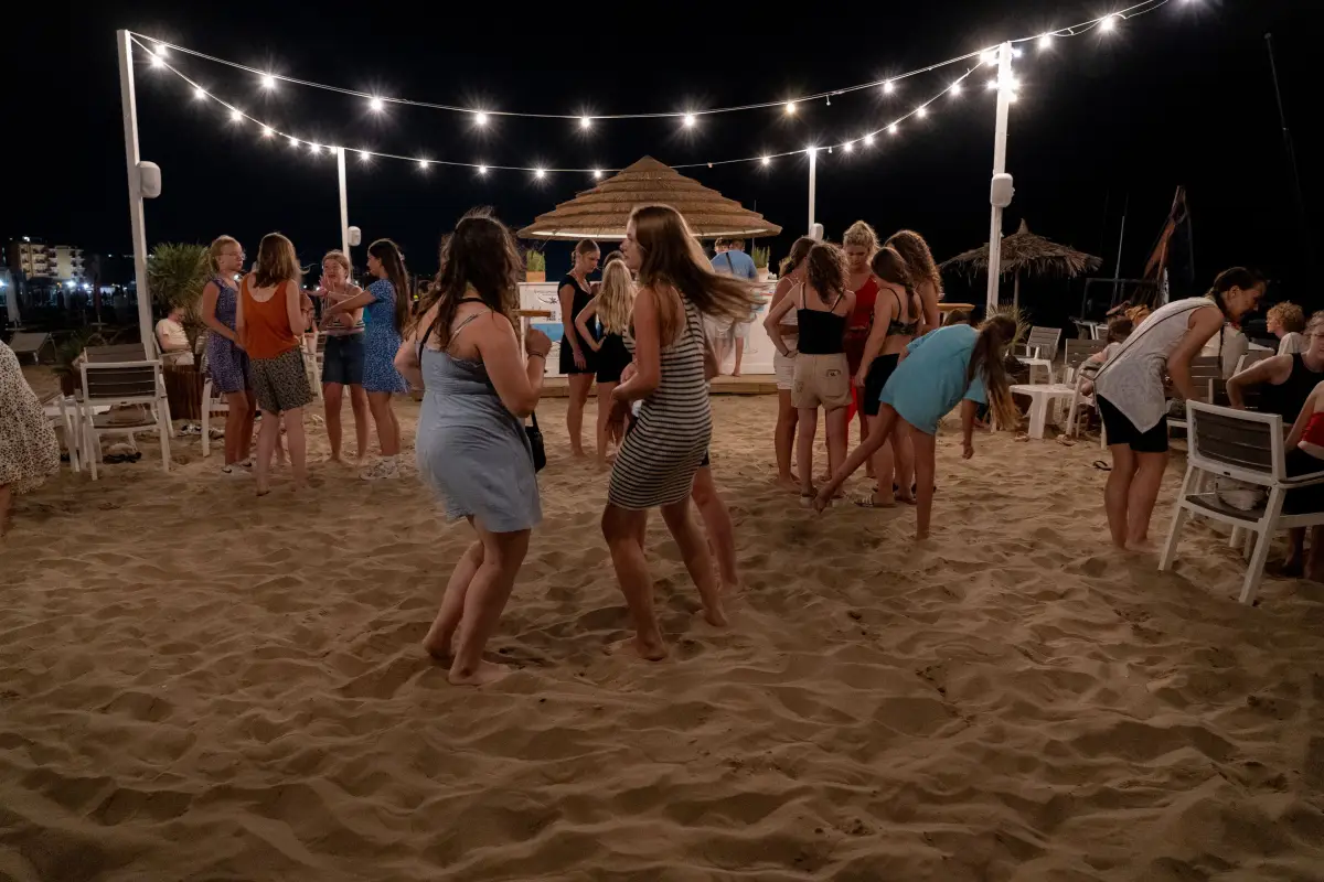 An evening beach party on the sand, with teenagers dancing under strings of lights