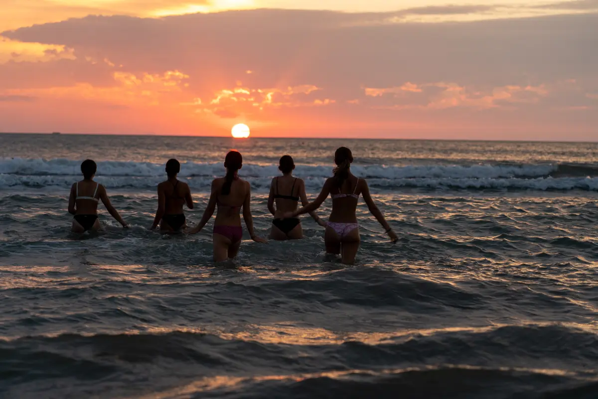 Participants standing in the shallow sea at sunset, in silhouette against the water