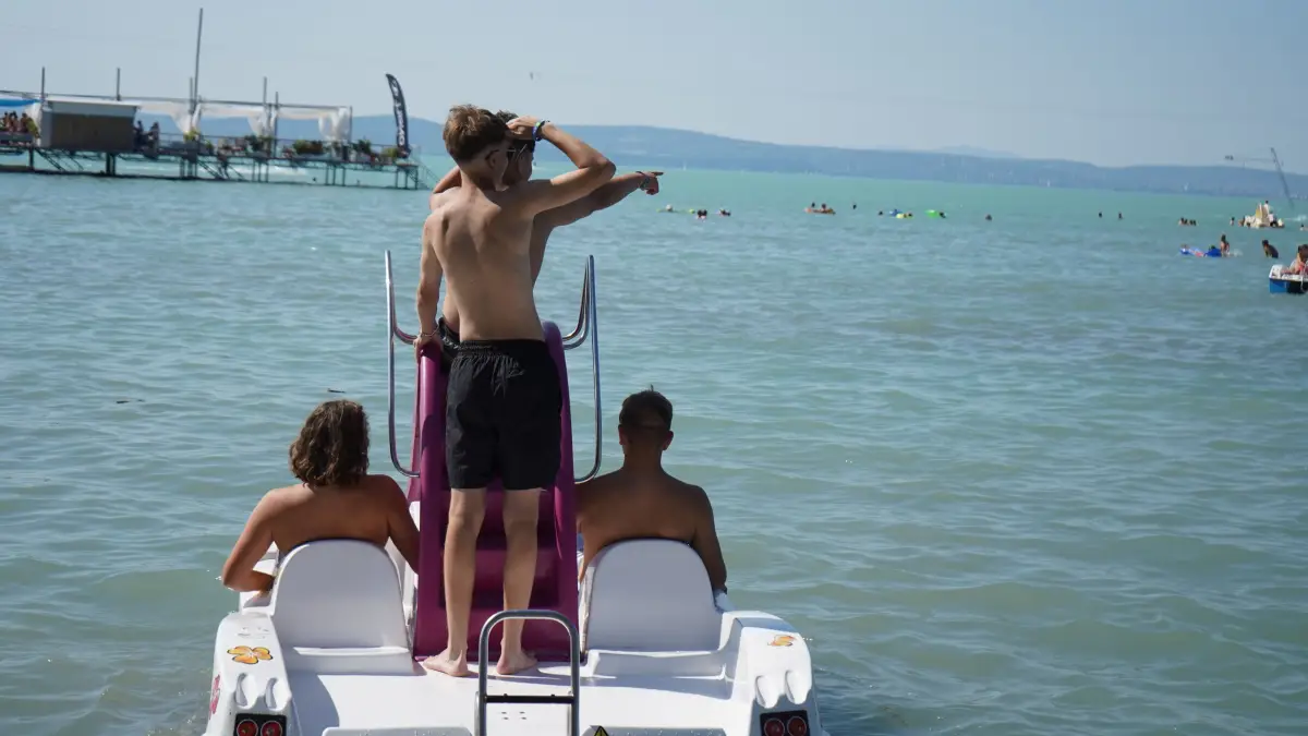 Teenagers on a pedalo with a slide in the shallow water, one of them standing on the top