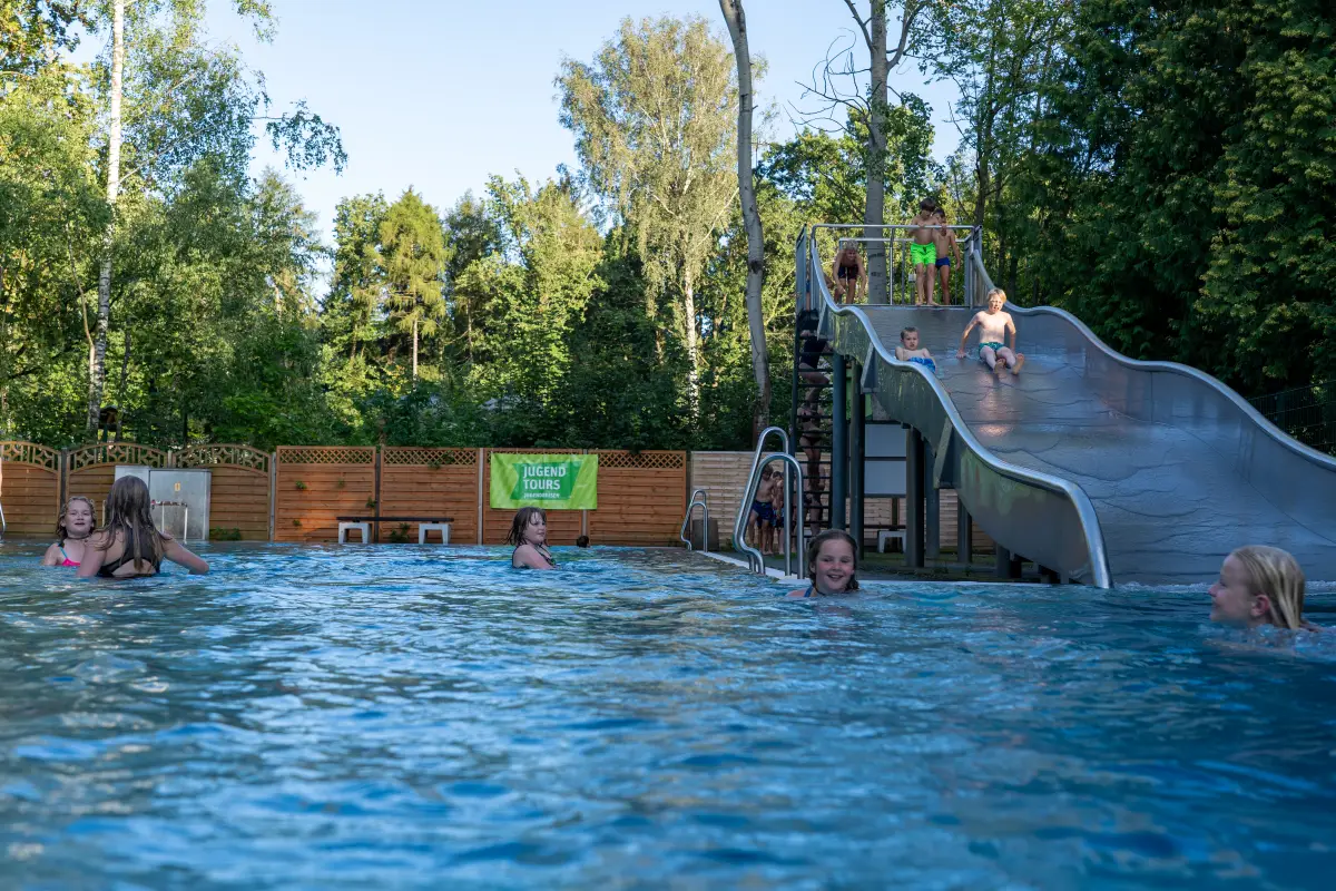Outdoor pool with a long slide, surrounded by trees