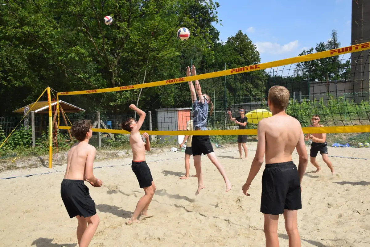 Teenagers playing beach volleyball on a sand court surrounded by trees