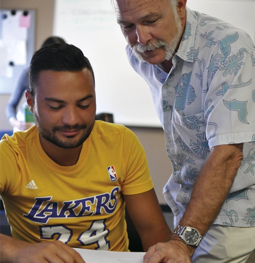 A teacher leaning over to help a student at his desk during a lesson at LSI San Diego.