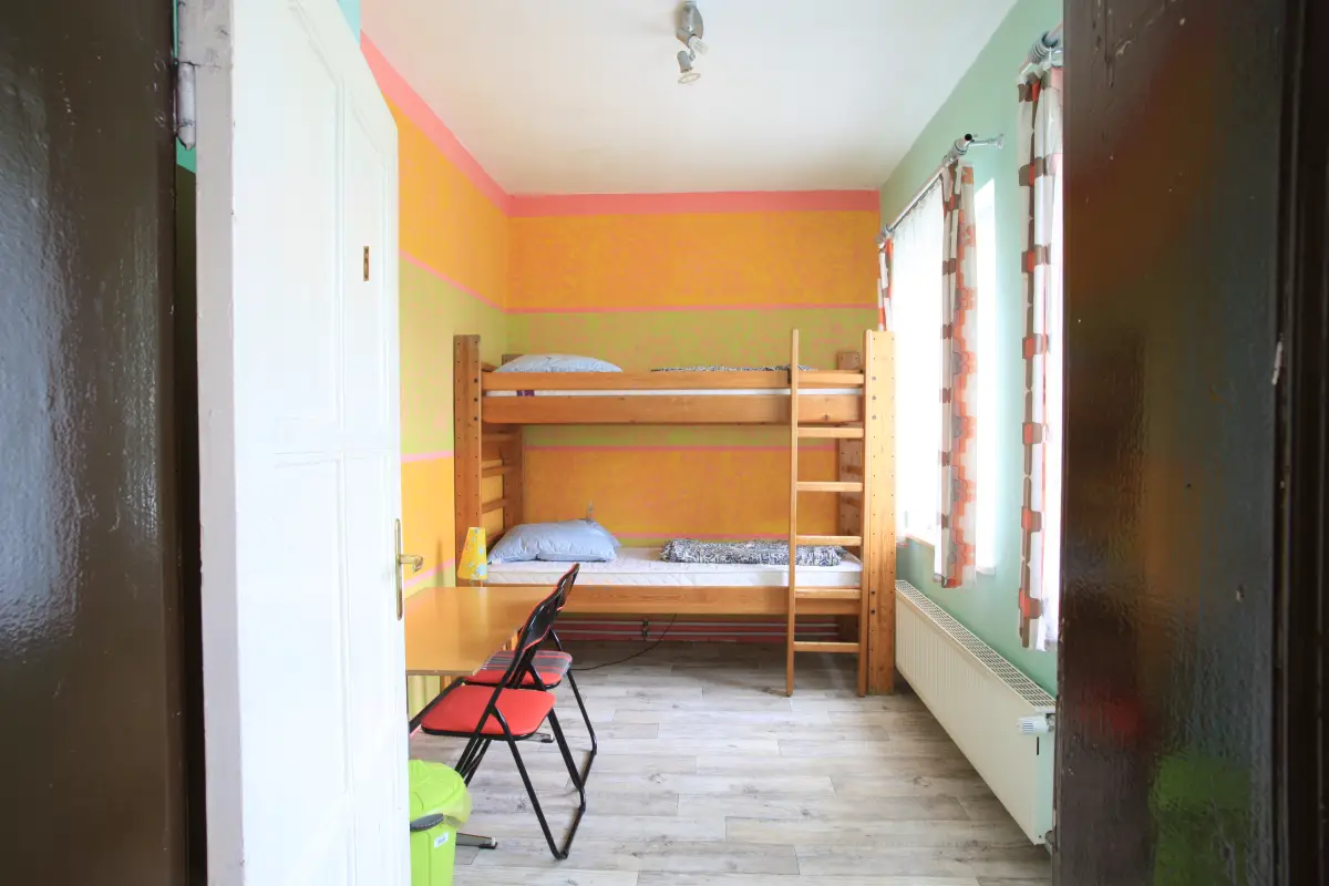 A second multi-bed room with a wooden bunk bed, a chair and a window onto the yard