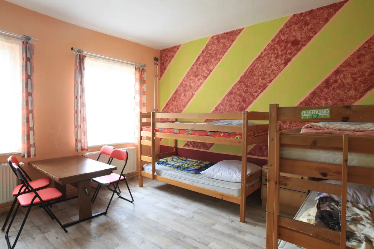 A multi-bed room with wooden bunk beds, a table and chairs and a striped painted wall