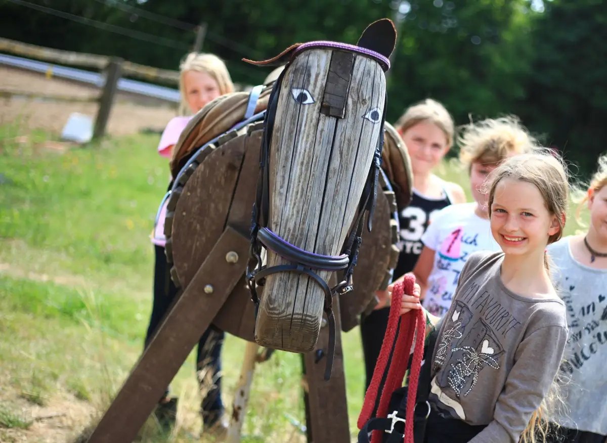 A home-made wooden hobby horse with a bridle held up in the paddock, with girls standing behind it