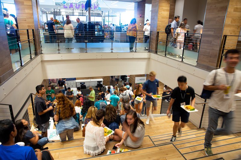 Students carrying trays in the two-storey campus dining hall at Georgetown