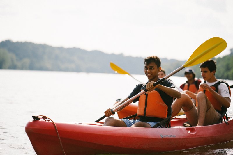 Students in life jackets paddling a red kayak on the Potomac River