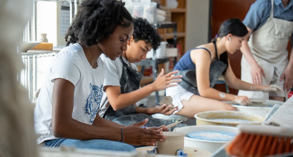 Students gathered round a table working clay by hand in the school ceramics studio