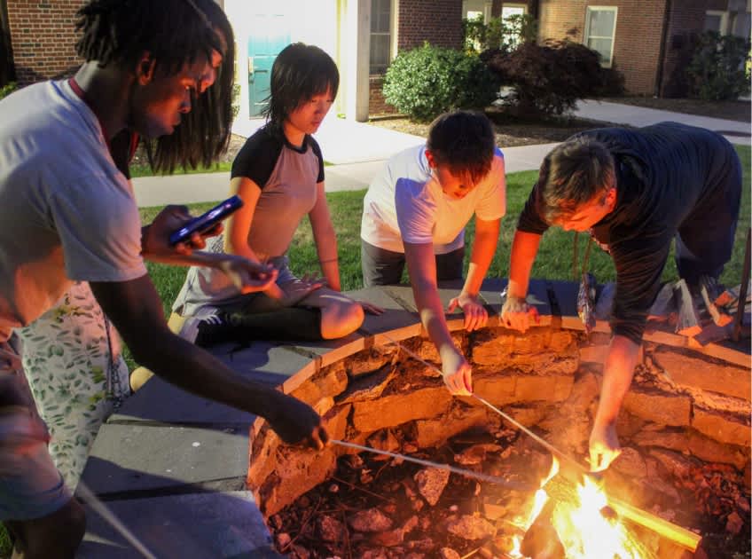 Students roasting marshmallows over a bonfire in the evening