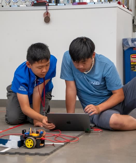 Two students sitting on the floor programming a device together