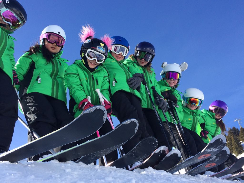 Campers in green Préfleuri ski jackets, helmets and goggles lined up with their skis on the snow