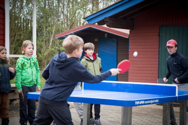Children playing table tennis at an outdoor table beside the wooden huts in Manderscheid