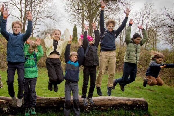 Campers jumping off a log on a meadow at the Manderscheid camp