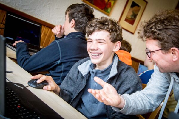 A camper laughing at a computer while a team member explains, during an IT session at the Manderscheid camp