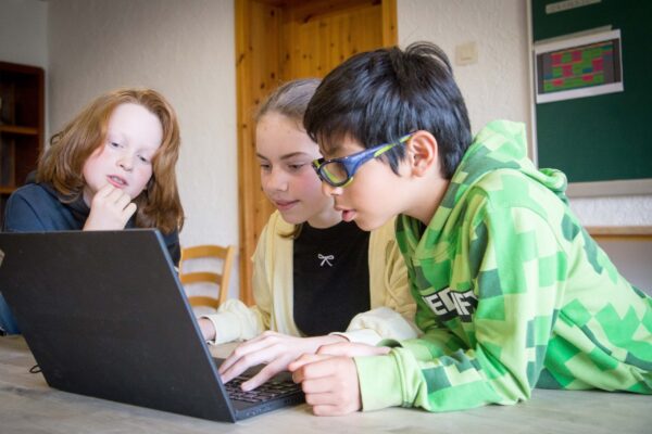 Three children working together on a laptop indoors at the Manderscheid camp