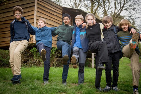 Group of children doing a high-kick pose on the grass in front of a wooden hut at the camp in Manderscheid