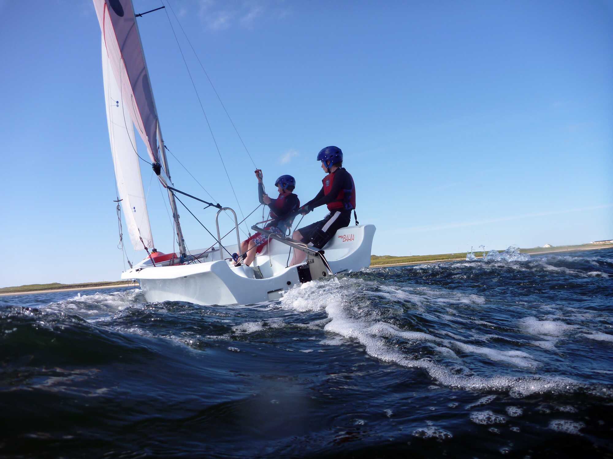Two students hiking out on the trapeze of a catamaran in strong wind.