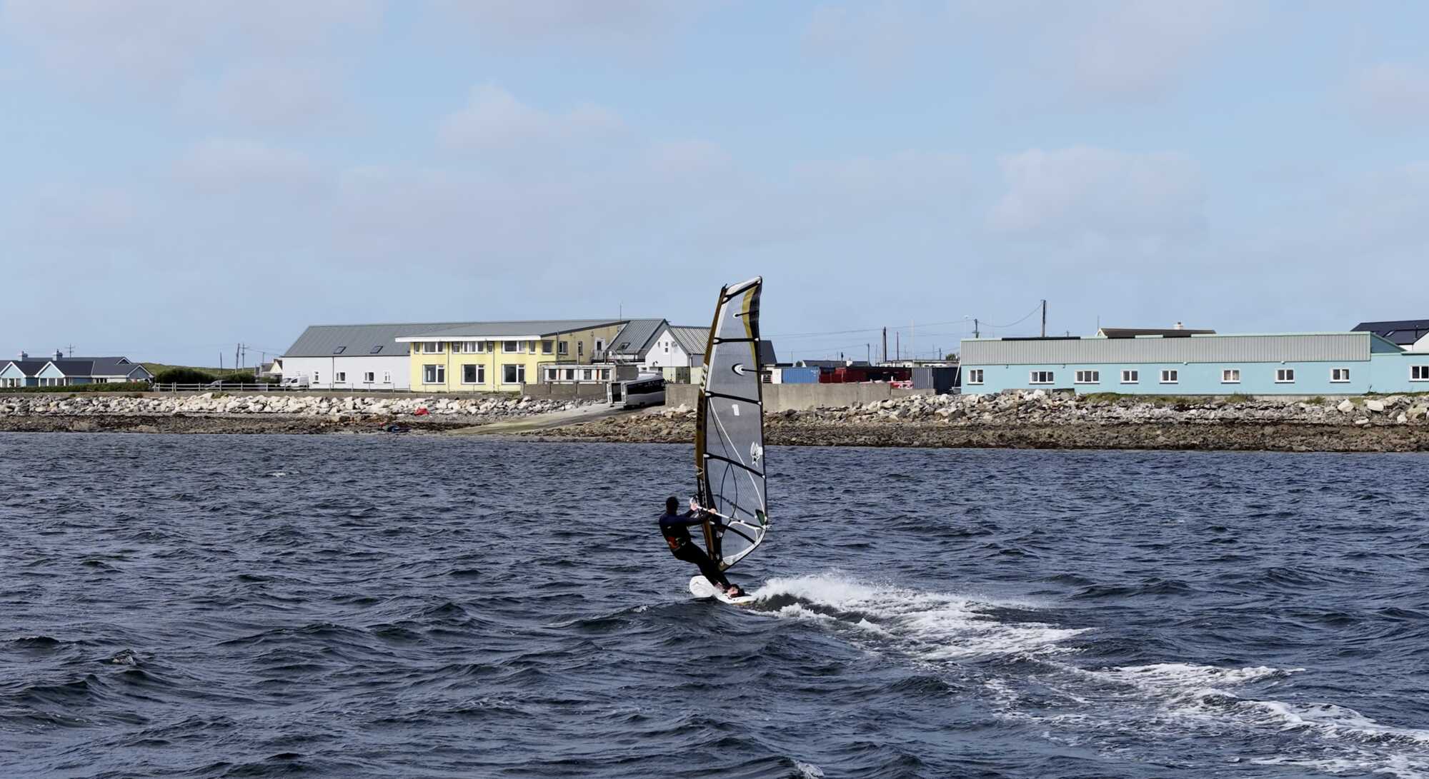 A windsurfer crossing the bay with the Coláiste UISCE buildings on the shore behind.