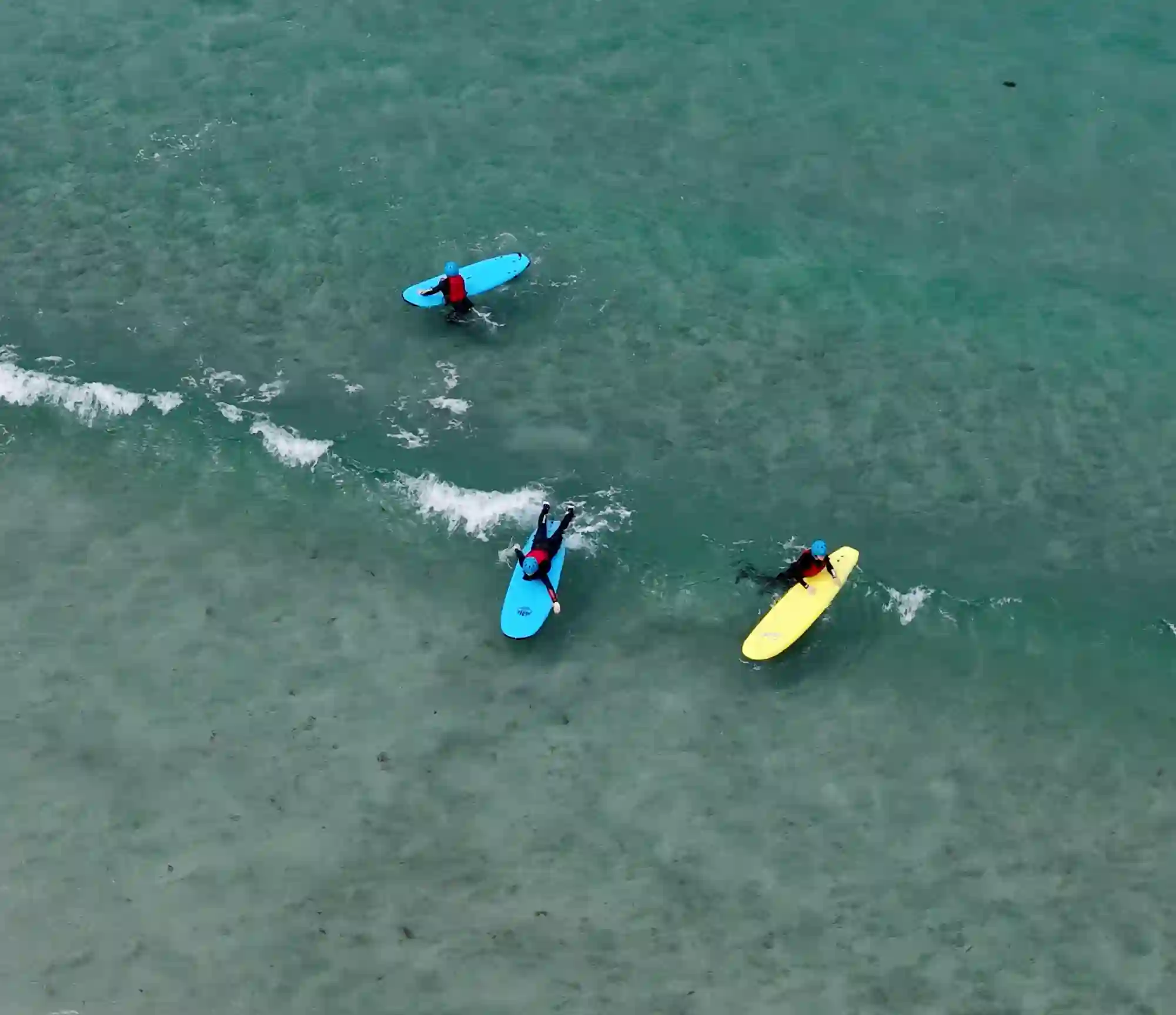 Students paddling out on surfboards in the turquoise water off the college beach.