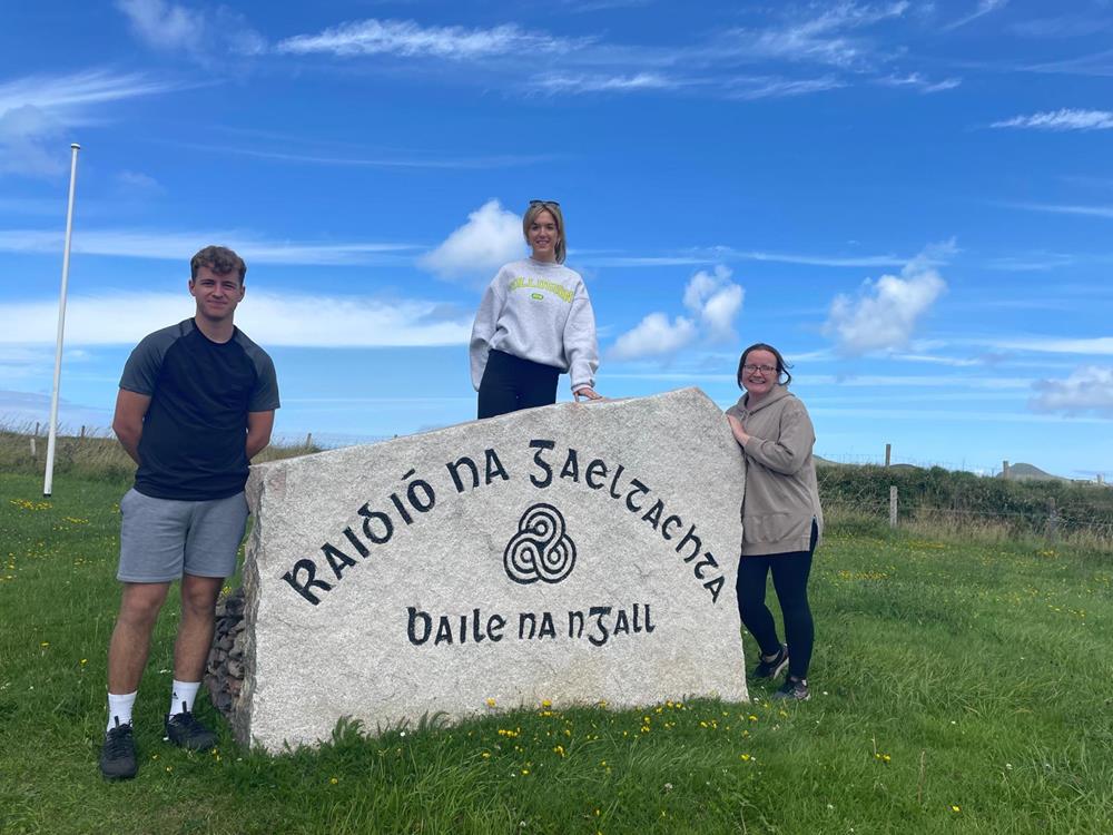 Students beside the carved stone marker of Raidió na Gaeltachta at Baile na nGall during an excursion