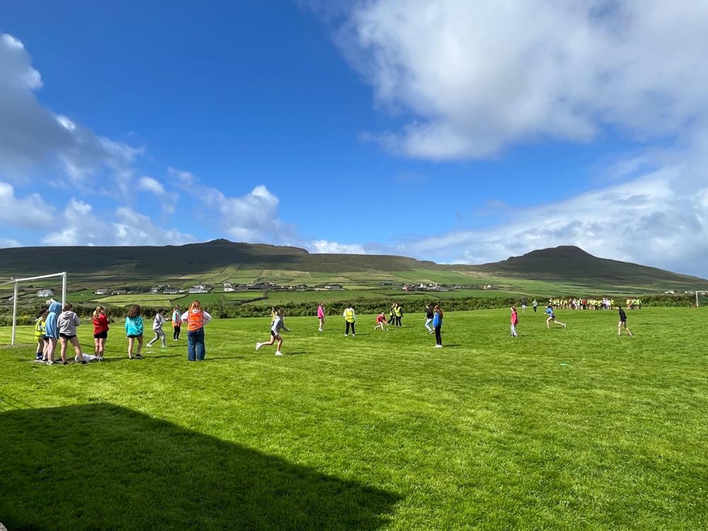 Students playing on a wide green sports field with the west Kerry hills behind
