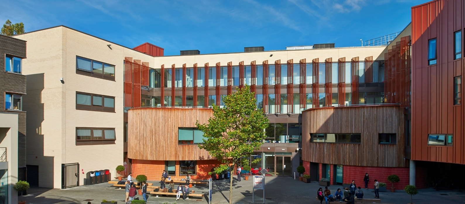 Courtyard of the Anglia Ruskin University campus in Cambridge, with modern buildings clad in timber and copper-coloured panels and students sitting at benches