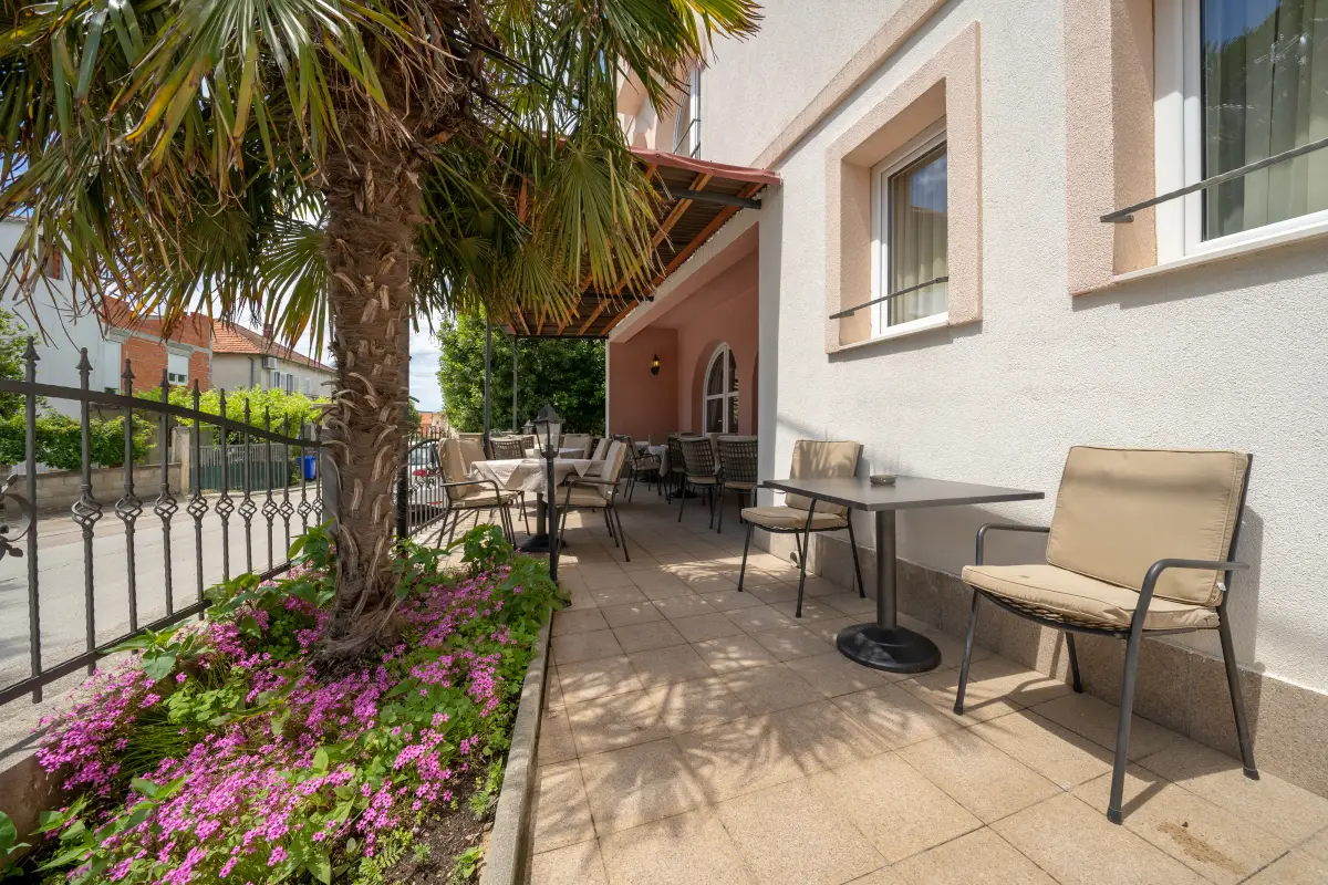 Garden seating area beside the hotel with armchairs, palms and flowering shrubs