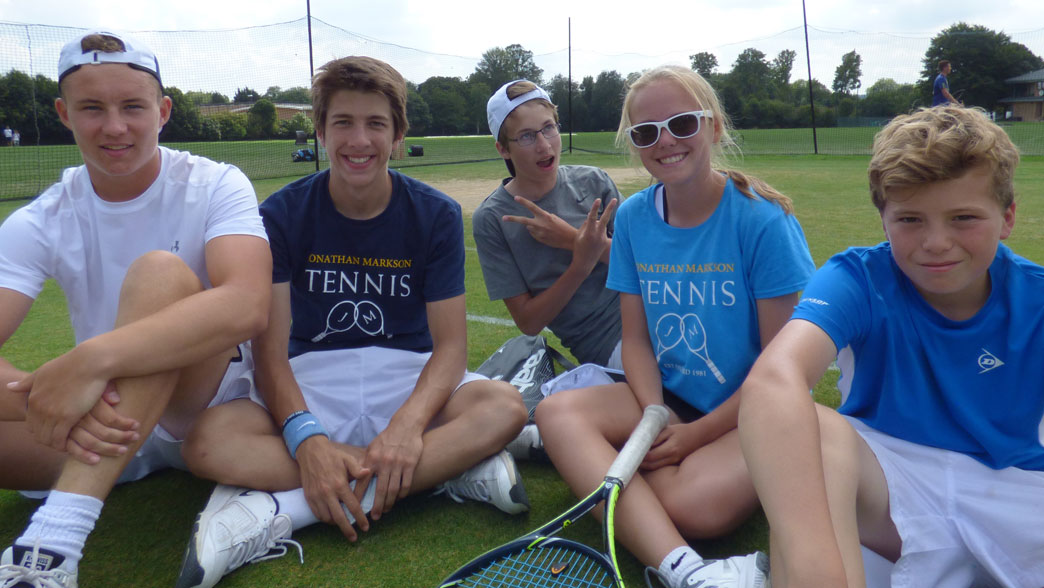 Group of teenage players sitting together with their rackets on the grass at the Oxford tennis camp
