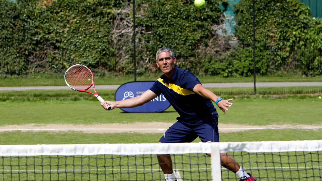 Coach playing a forehand at the net during a drill on the grass courts at Oxford