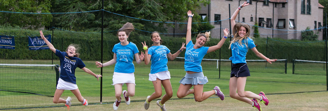 Group of girl players in camp shirts jumping in the air on court at the Oxford tennis camp