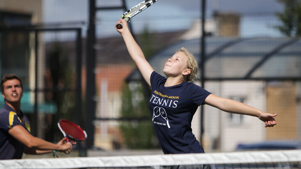 Young player stretching up to hit a smash on court at the Oxford tennis camp