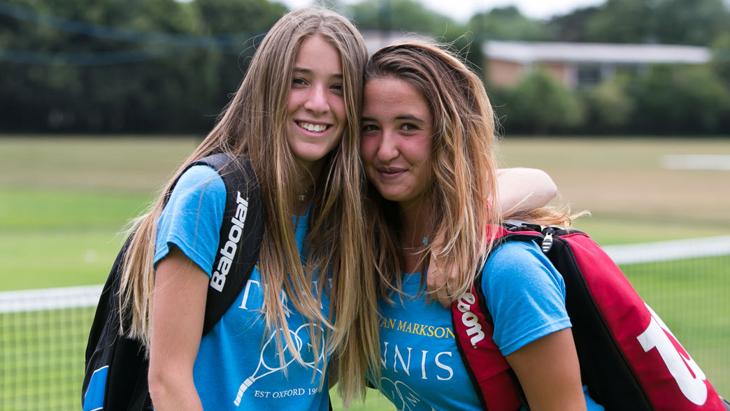 Two teenage players in camp shirts carrying their racket bags at the Oxford tennis camp