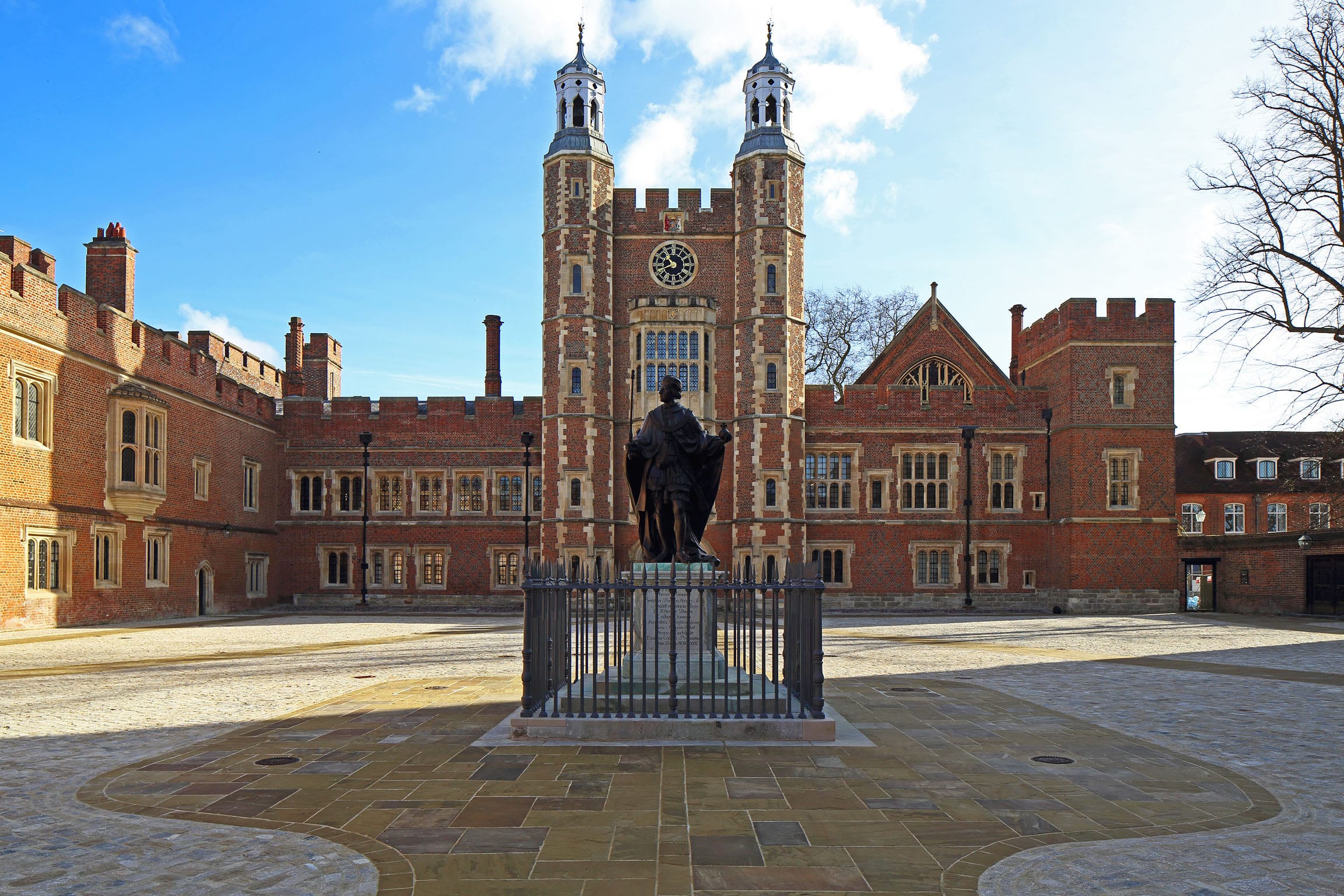 The red-brick quadrangle of Eton College in Windsor, with its clock tower and the statue of the founder behind railings