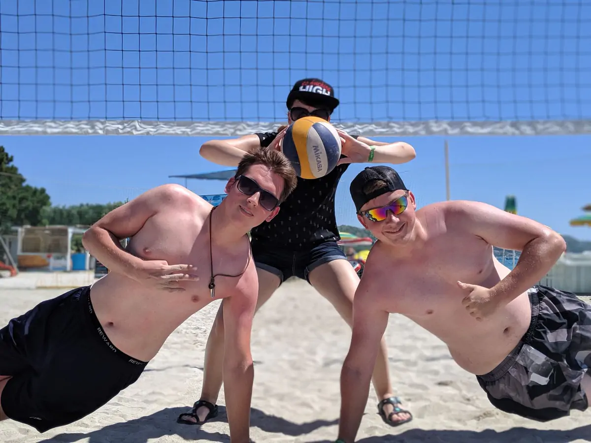 Three participants posing with a ball on the beach volleyball court
