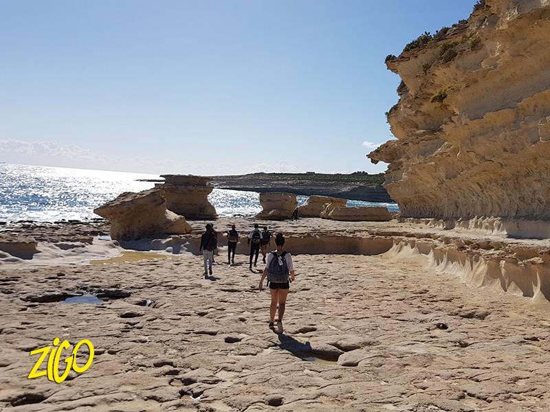 Young people walking across a flat shelf of coastal limestone below a cliff face
