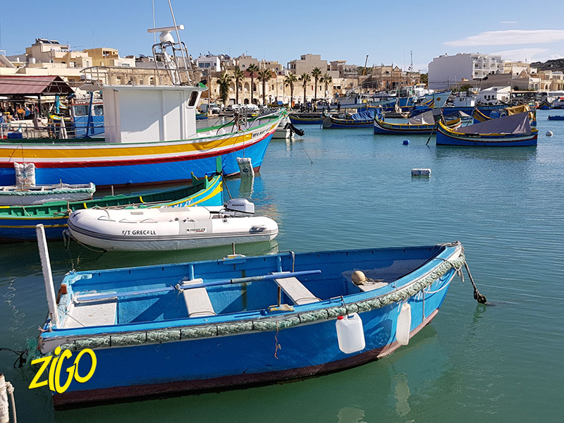 Painted wooden fishing boats moored in the harbour of Marsaxlokk in front of the village houses
