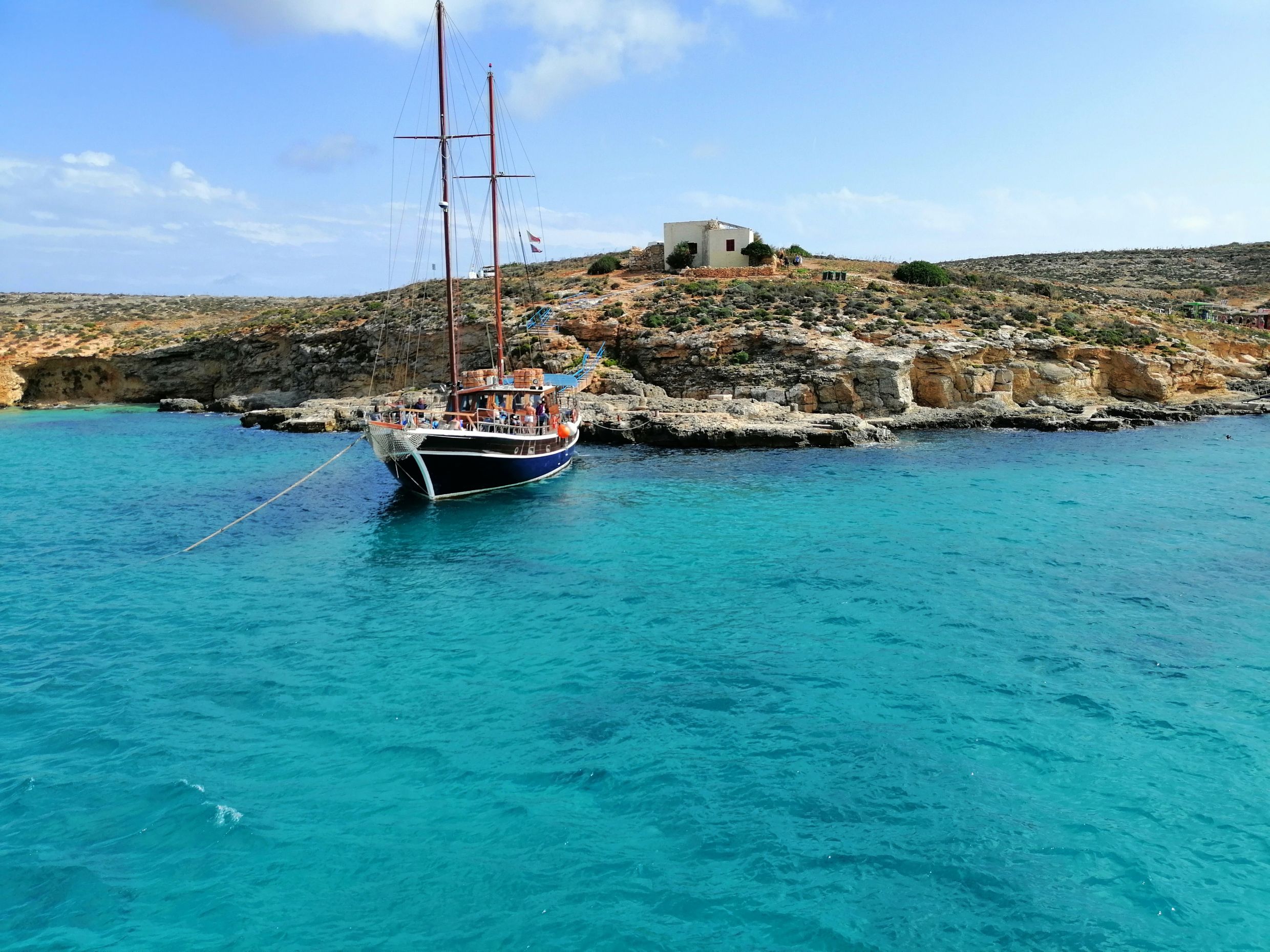 Sailing boat anchored in a turquoise bay beside a low rocky island
