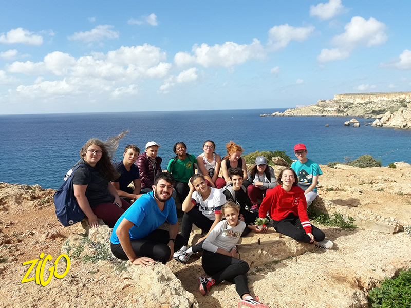 Group of young people sitting together on rocks on a headland above the sea