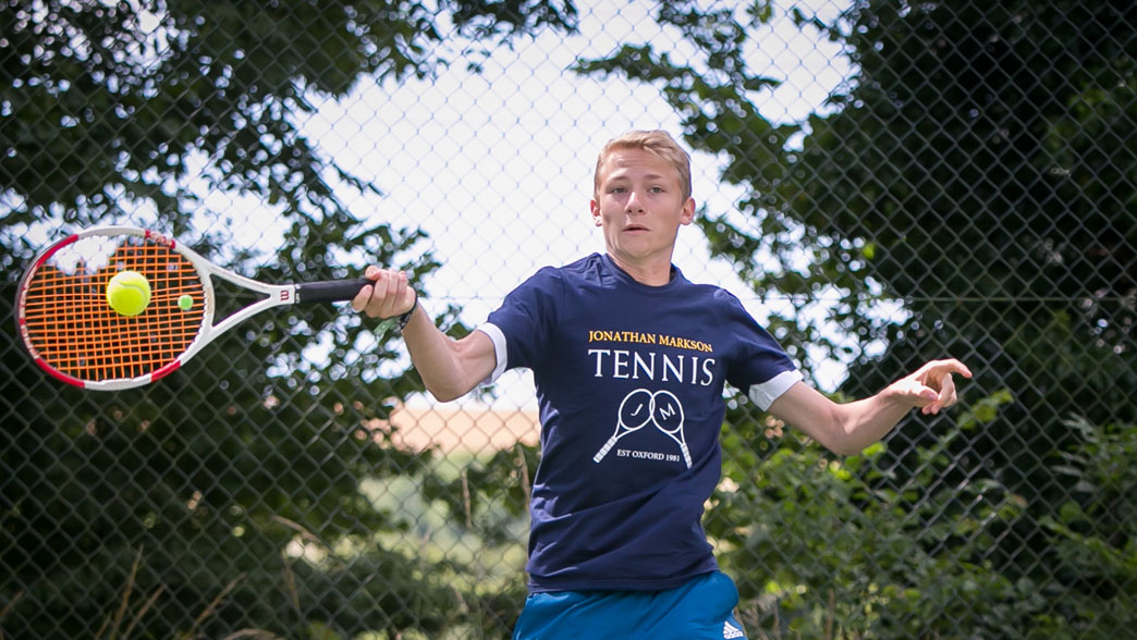 Player hitting a forehand beside the court fence at the Brighton tennis camp