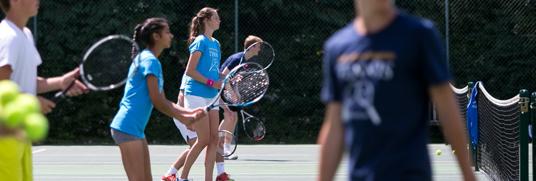 Players in camp shirts lined up with their rackets beside the net at the Brighton tennis camp