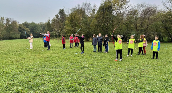 Children in coloured team bibs lined up across the meadow at the Manoir du Viginet centre, several taking aim with bows