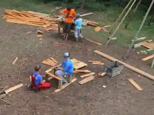 Children sorting and cutting boards and beams for the tree house on the forest building site