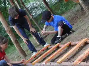 Three children laying out wooden rungs to build a ladder for the tree house