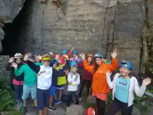 Children with helmets cheering at a rock wall during the cave hike in the Langenhennersdorf rock labyrinth