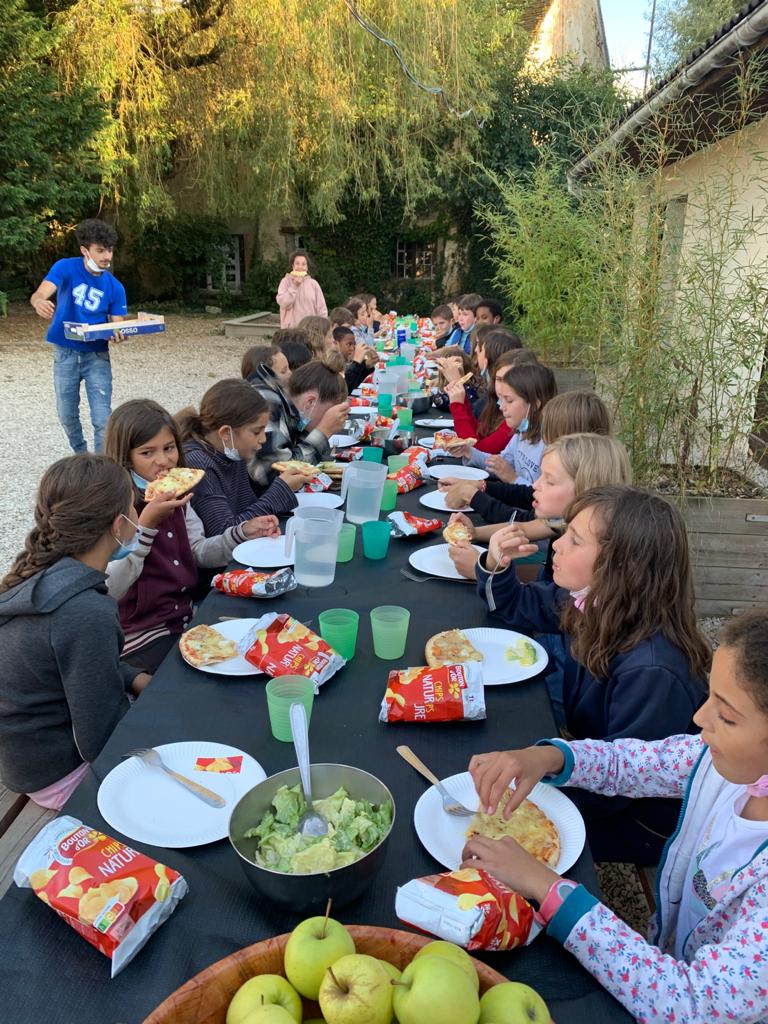 Children eating together at a long table laid outdoors under the trees at Domaine de Chevillon