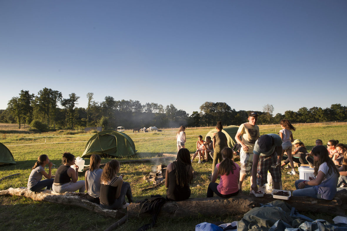 Children sitting together around a fire beside the tents at dusk during a bivouac in the countryside