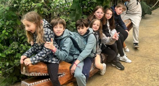 A group of children sitting together on a bench among greenery during the zoo visit