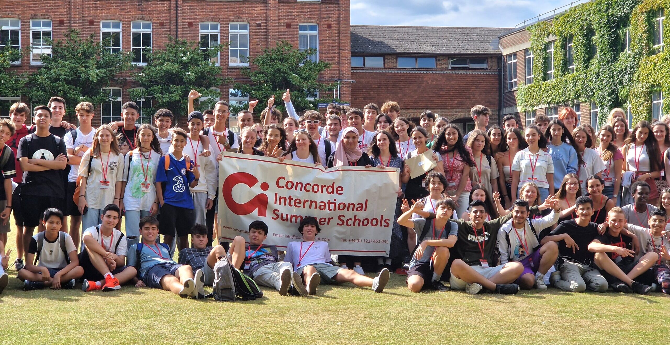 Large group photo of summer school students on the lawn holding a Concorde International Summer Schools banner at Ashford School, Ashford, Kent