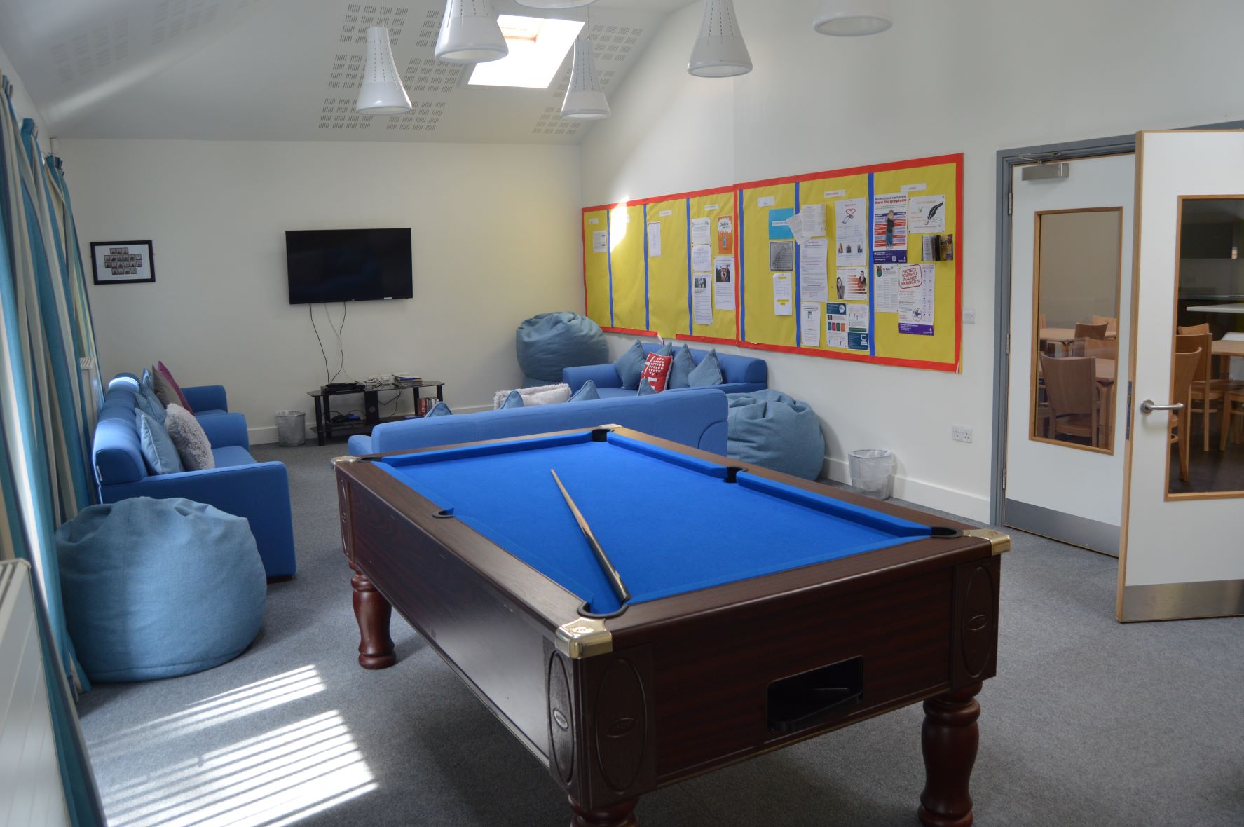 Common room with a pool table, soft seating, a television and a noticeboard at Ashford School, Ashford, Kent
