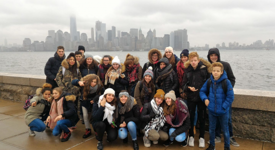 The group of teenagers posing in winter coats with the Lower Manhattan skyline behind them